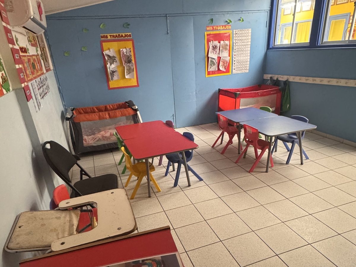 Sala con paredes azules, mesas pequeñas y alfombra roja de actividades
